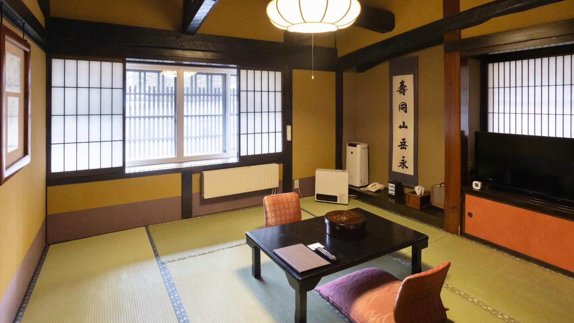 Um quarto japonês tradicional com tatames, uma mesa baixa, uma televisão e uma porta deslizante com vista para o exterior.