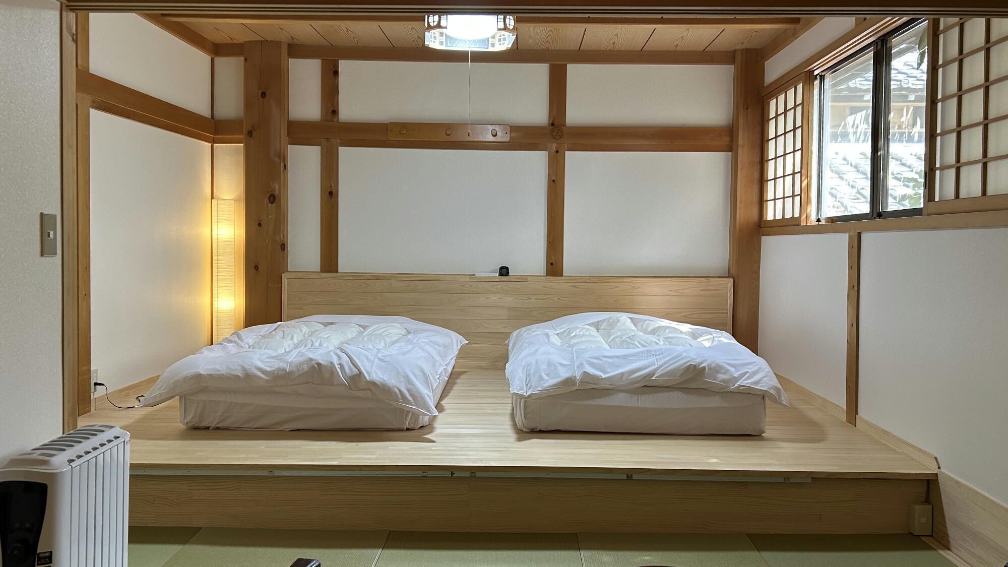 A room with a low wooden bed frame, a small bedside table, and a window with a view.