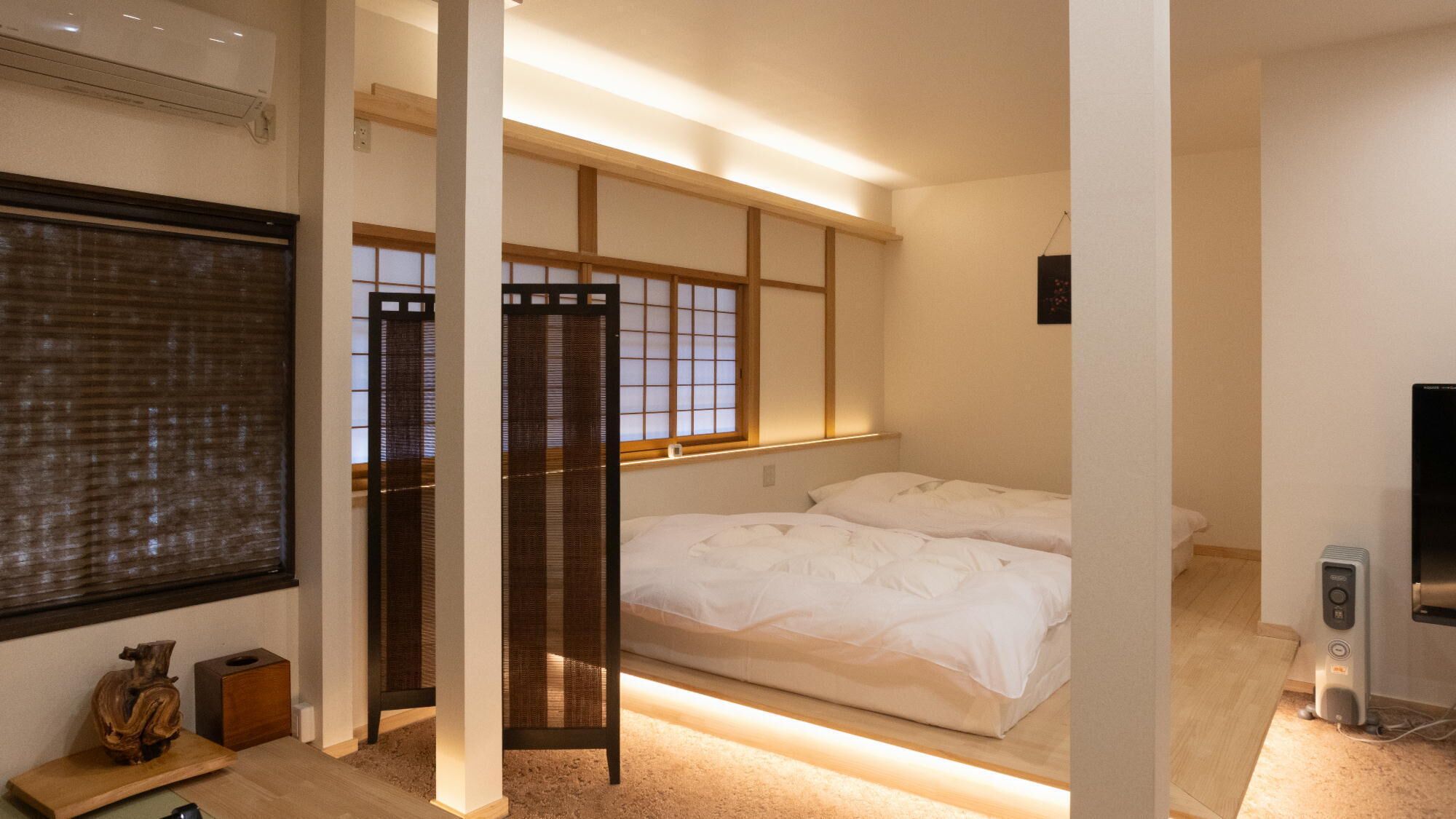 A traditional Japanese-style bedroom with tatami flooring, a low bed, a shoji screen, and a television.