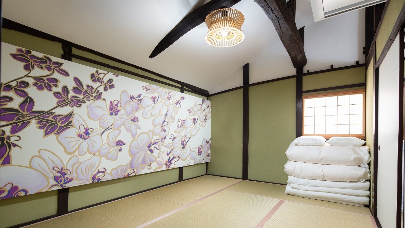 A traditional Japanese room with tatami flooring, a floral wall hanging, and a stack of white bedding.