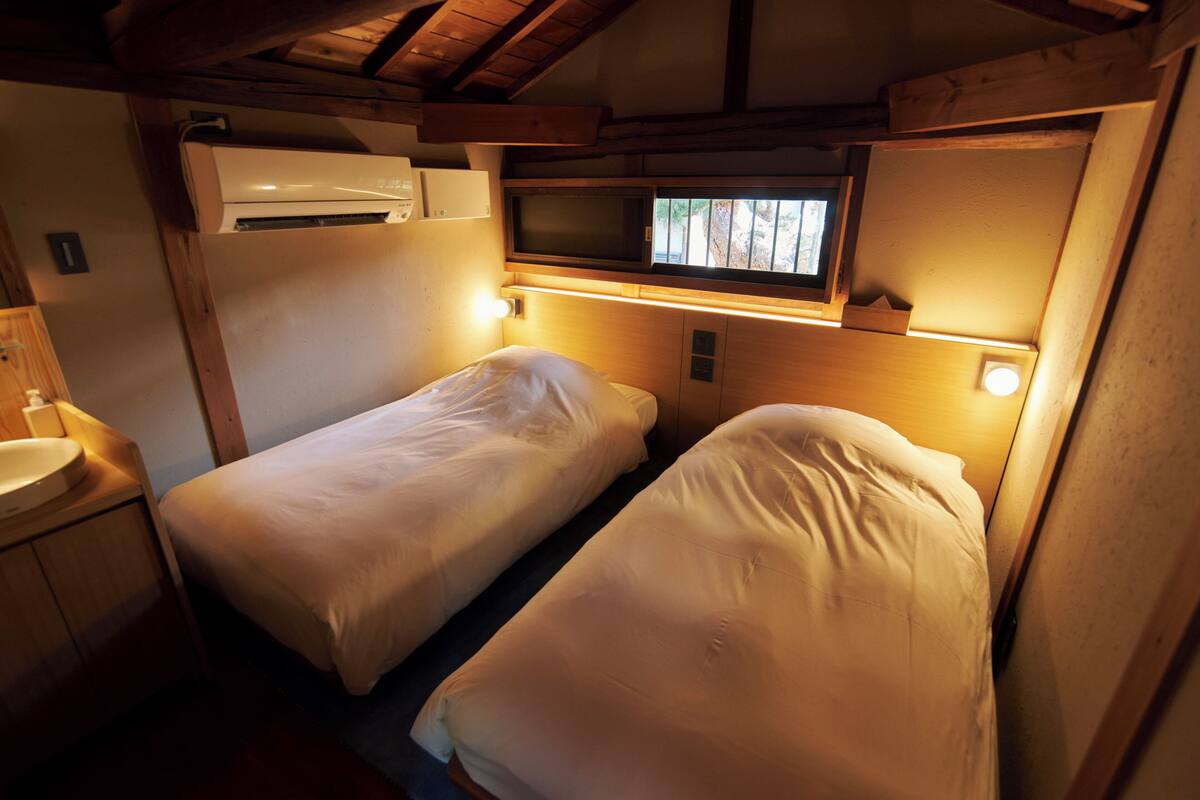 Una habitación compacta con dos camas individuales, aire acondicionado integrado, microondas y una ventana pequeña.