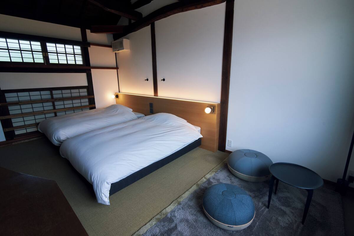 Un dormitorio tradicional japonés con suelo de tatami, una cama baja sobre plataforma y un biombio shoji.