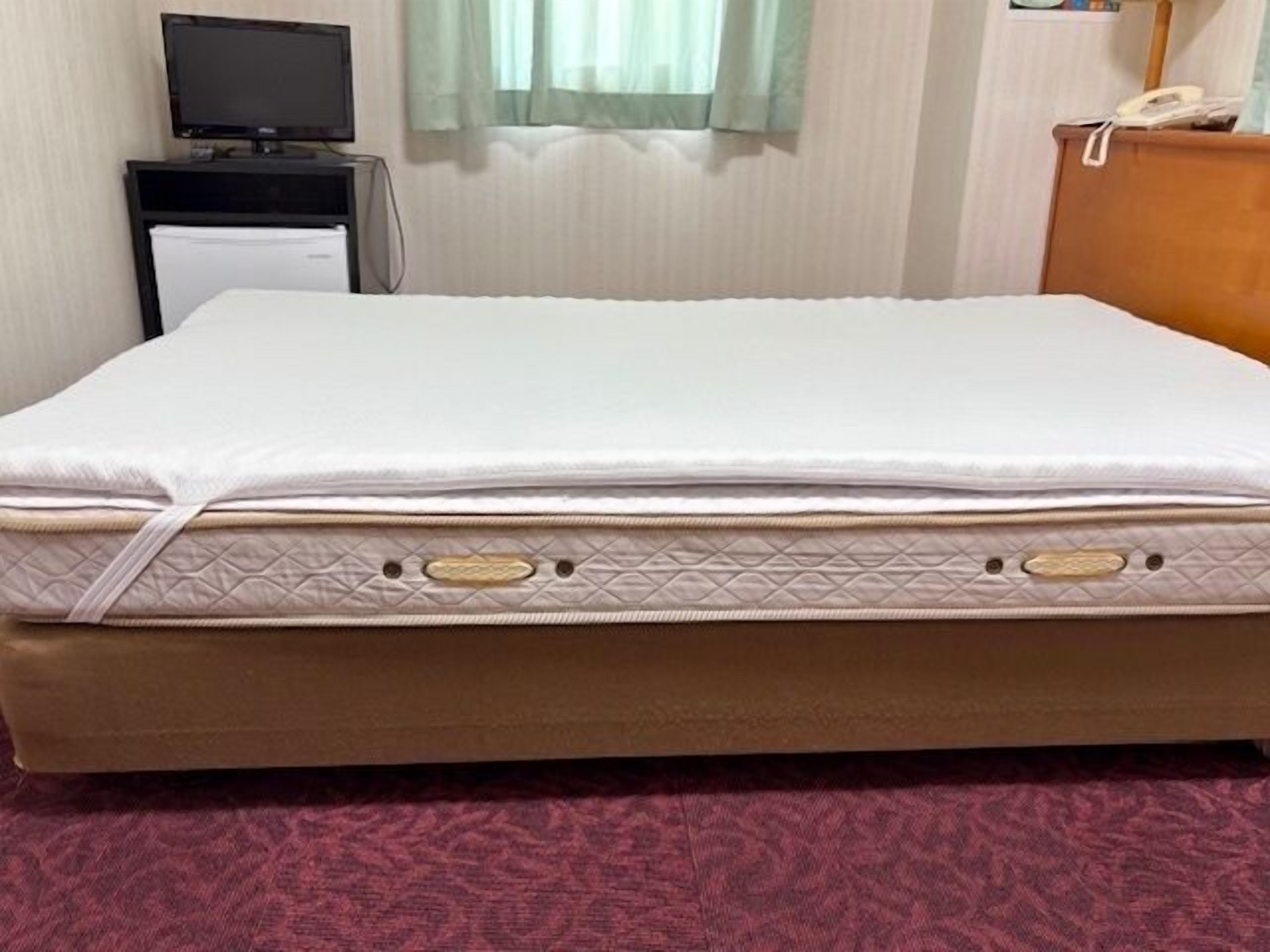 A bed with a quilted mattress, a bedside table with a telephone, and a television on a stand.