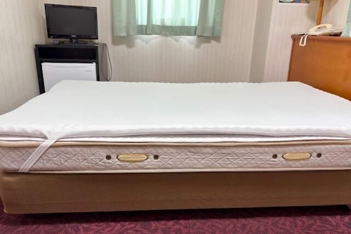 Una cama con colchón acolchado, una mesita de noche con teléfono y un televisor sobre un mueble.