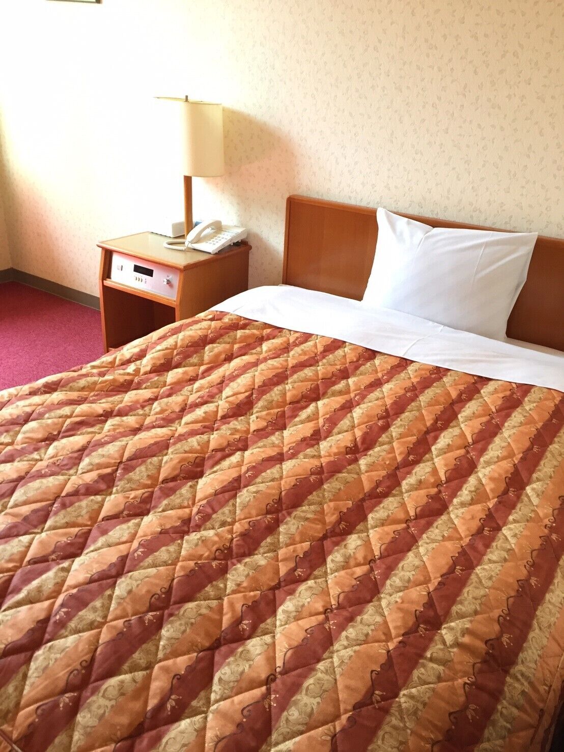 A hotel room with a bed, a nightstand with a lamp, and a telephone.