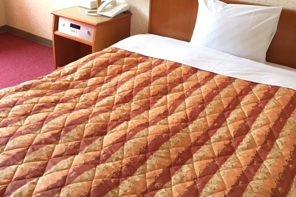 Una habitación de hotel con una cama, una mesita de noche con lámpara y un teléfono.