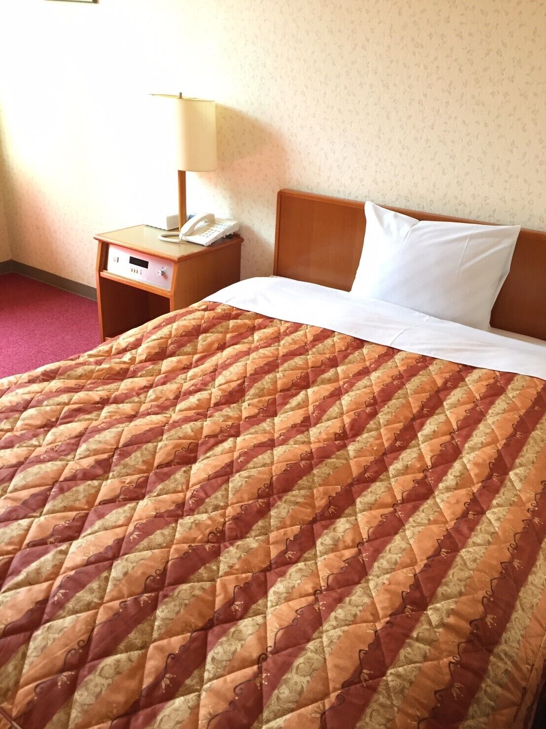 A hotel room with a bed, a nightstand with a lamp, and a telephone.