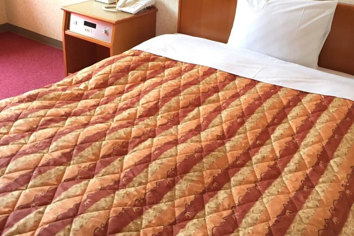 A hotel room with a bed, a nightstand with a lamp, and a telephone.