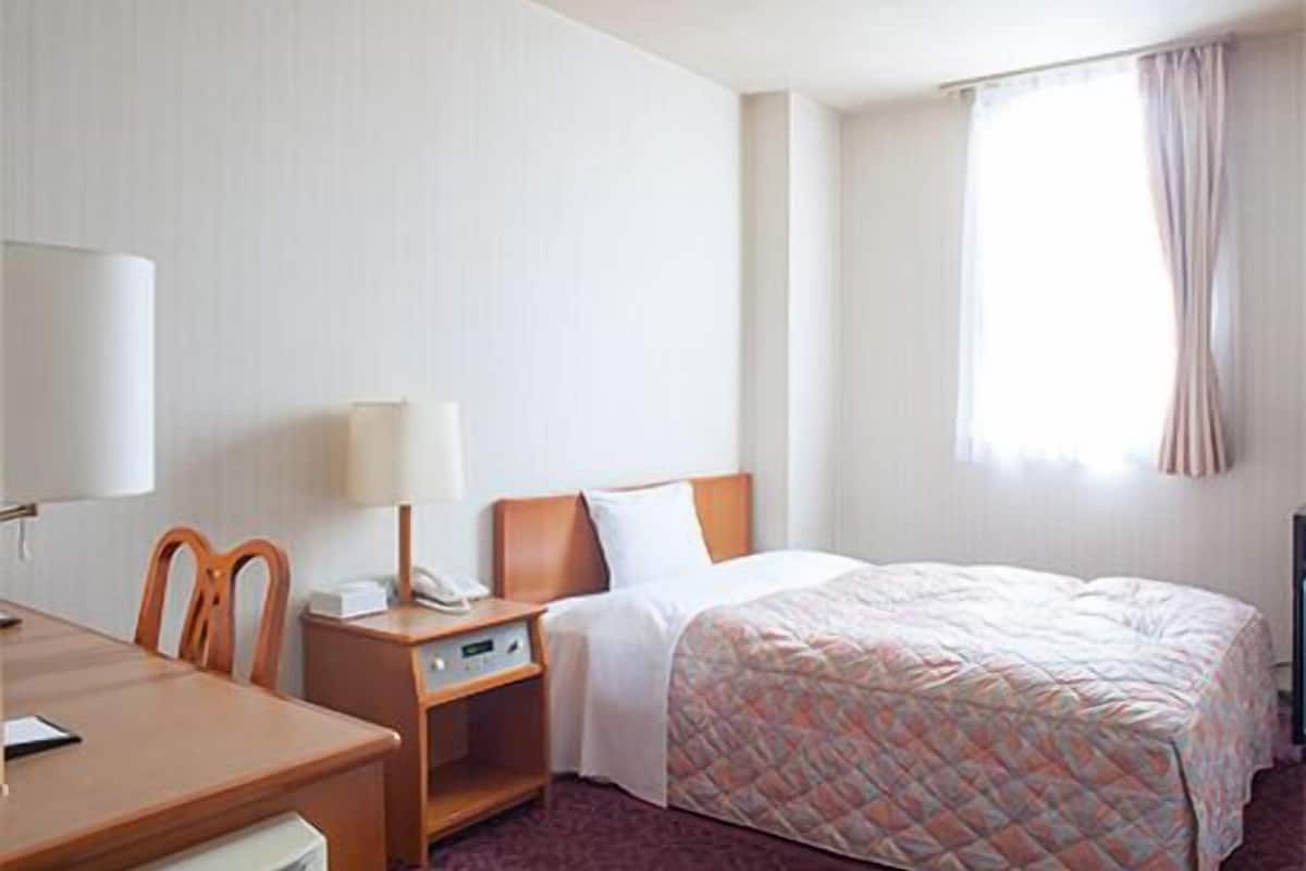 Una habitación de hotel con una cama, un escritorio con lámpara, una silla y un teléfono.