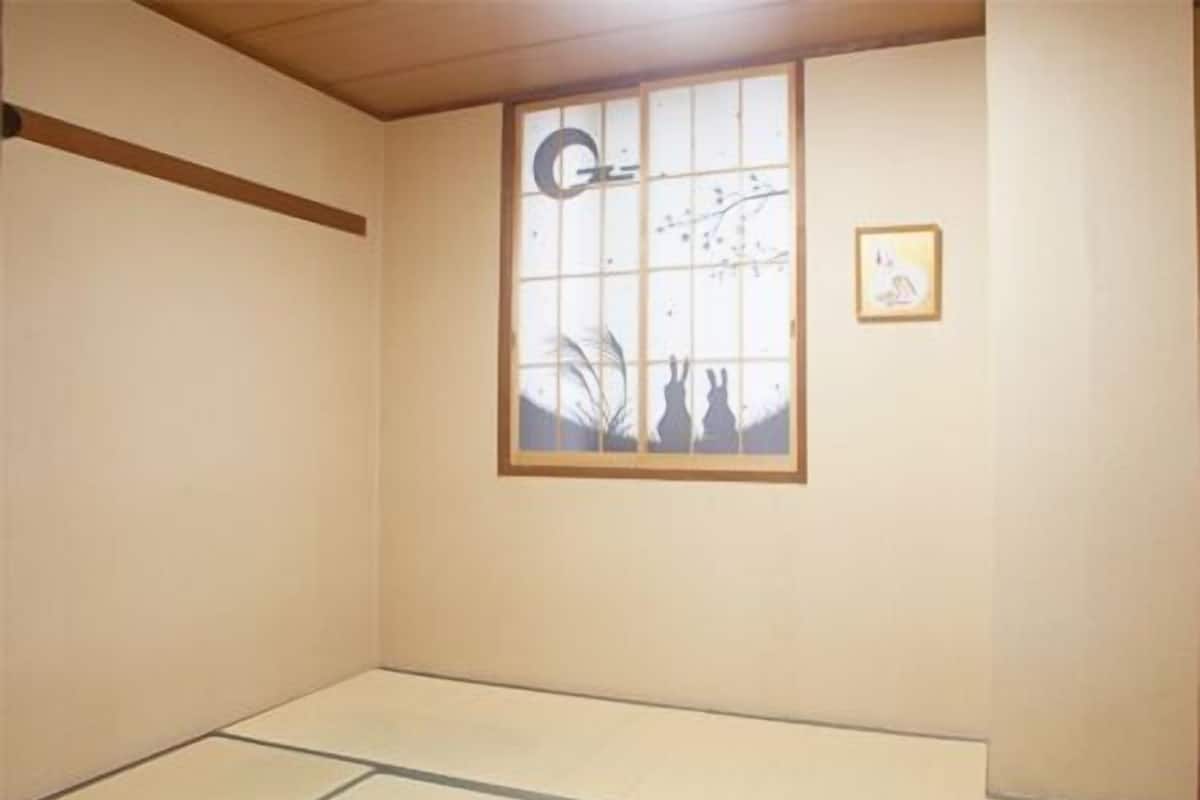 Una habitación con suelo de tatami, ventana con pantalla shoji y un cuadro en la pared.