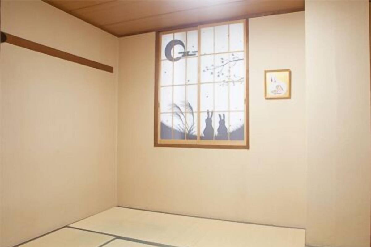 Una habitación con suelo de tatami, ventana con celosía de papel y un cuadro en la pared.