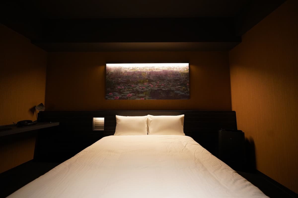 Quarto de hotel com cama, mesa de cabeceira, televisão fixada na parede e janela com vista para a paisagem.
