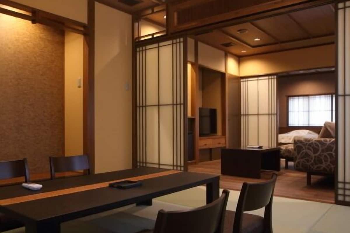 Quarto em estilo japonês tradicional, com tatames, uma mesa baixa, cadeiras, cama e portas deslizantes.