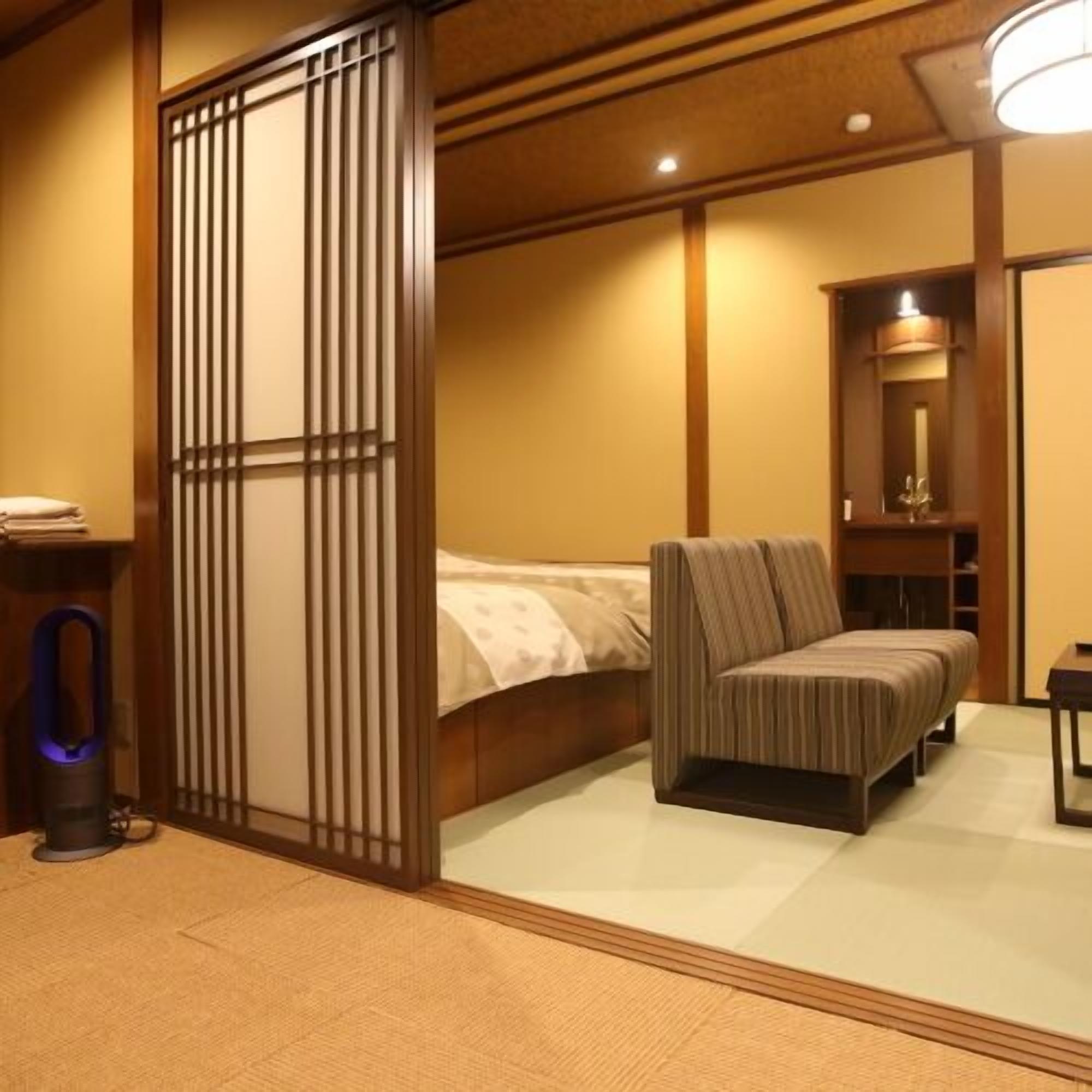 A room with a bed, a chair, a small table, and a partition with vertical slats.