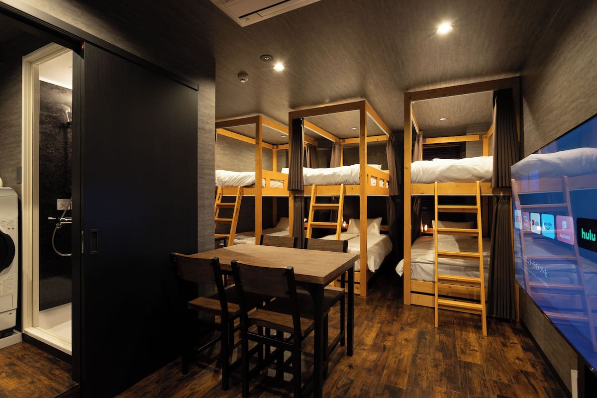 A room with bunk beds, a wooden table, and chairs, and a television displaying Hulu.