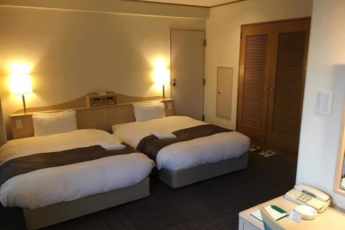 Una habitación de hotel con dos camas, un escritorio con teléfono y una puerta con interruptor de luz.