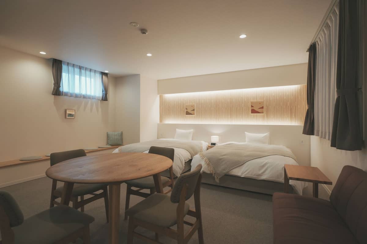 A hotel room with a round wooden table, two beds, a sofa, and a small table.