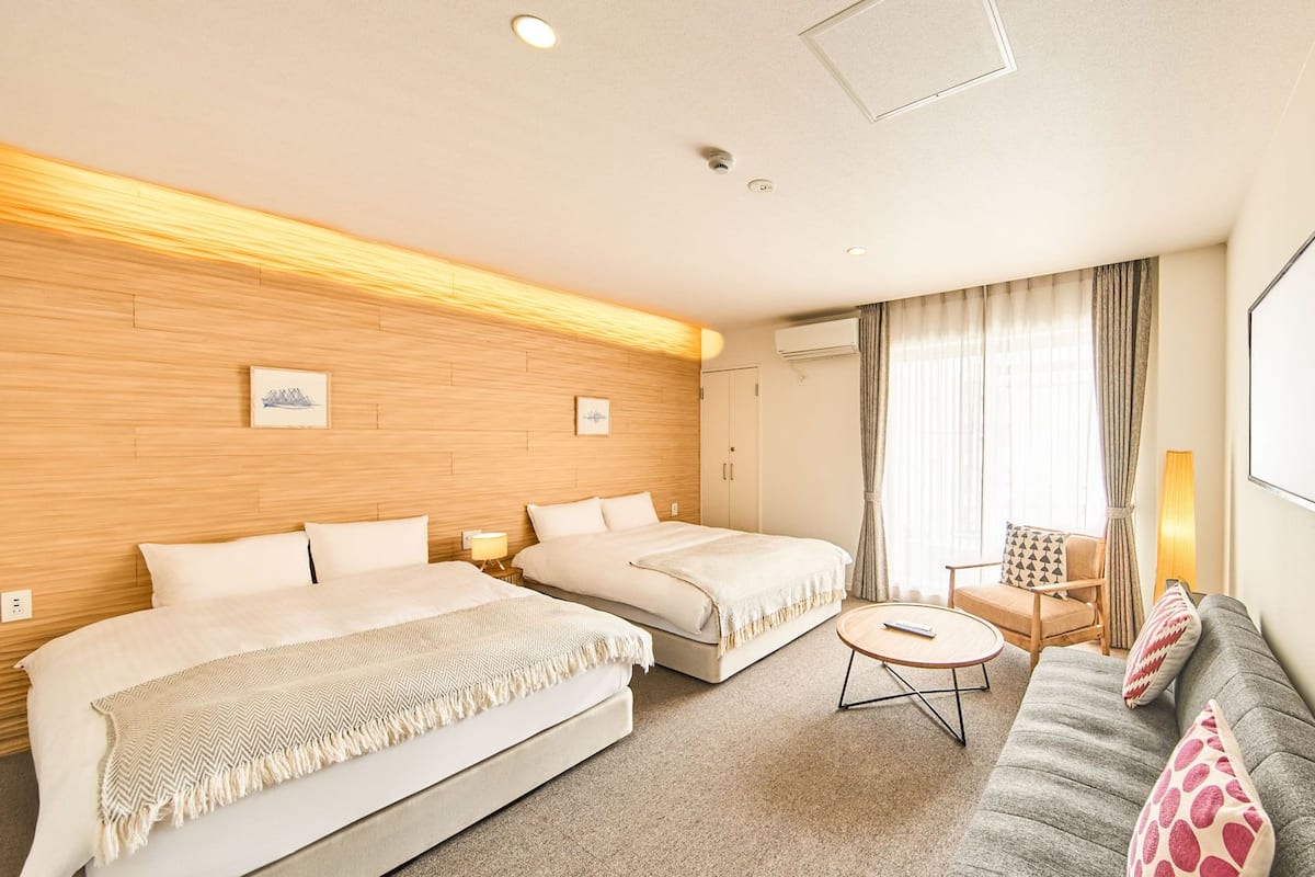 A hotel room with two beds, a sofa, a small table, and a TV mounted on the wall.