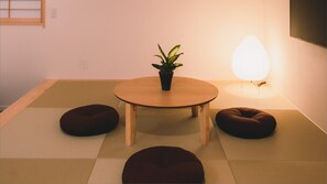 A room with tatami flooring, a round wooden table, a potted plant, and two bean bag chairs. - Nagi Hiroshima Hotel & Lounge (Hiroshima)