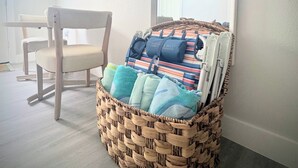 A room with a wicker basket containing towels and a striped bag, a wooden chair, and a large mirror on the wall. - Sandbar Suite | Coastal 1BR • Minutes to Beach (St. Augustine)