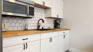 A kitchen with white cabinets, a microwave, a toaster, a sink, and a coffee maker. - Sandbar Suite | Coastal 1BR • Minutes to Beach (St. Augustine)