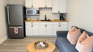 A modern kitchen with white cabinets, a stainless steel refrigerator, a microwave, and a coffee maker. - Sandbar Suite | Coastal 1BR • Minutes to Beach (St. Augustine)