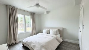 A bedroom with a bed, a ceiling fan, and a window with curtains. - Sandbar Suite | Coastal 1BR • Minutes to Beach (St. Augustine)