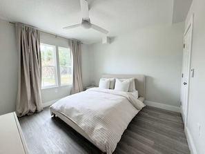 Ein Schlafzimmer mit Bett, Deckenventilator und einem Fenster mit Vorhängen.