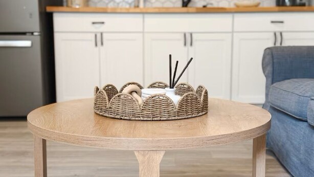 A round wooden table with a woven basket and incense sticks, a kitchen with white cabinets and a microwave, and a gray sofa in the background. - Sandbar Suite | Coastal 1BR • Minutes to Beach (St. Augustine)