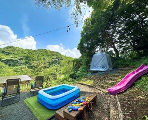 Un jardin avec une piscine gonflable bleue, un toboggan violet et une tente.