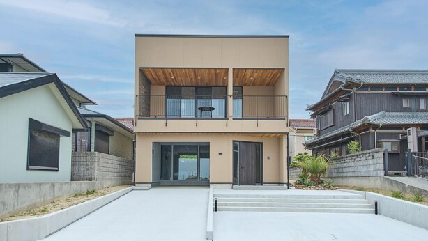 A modern two-story house with a balcony, a front door, and a small garden area.