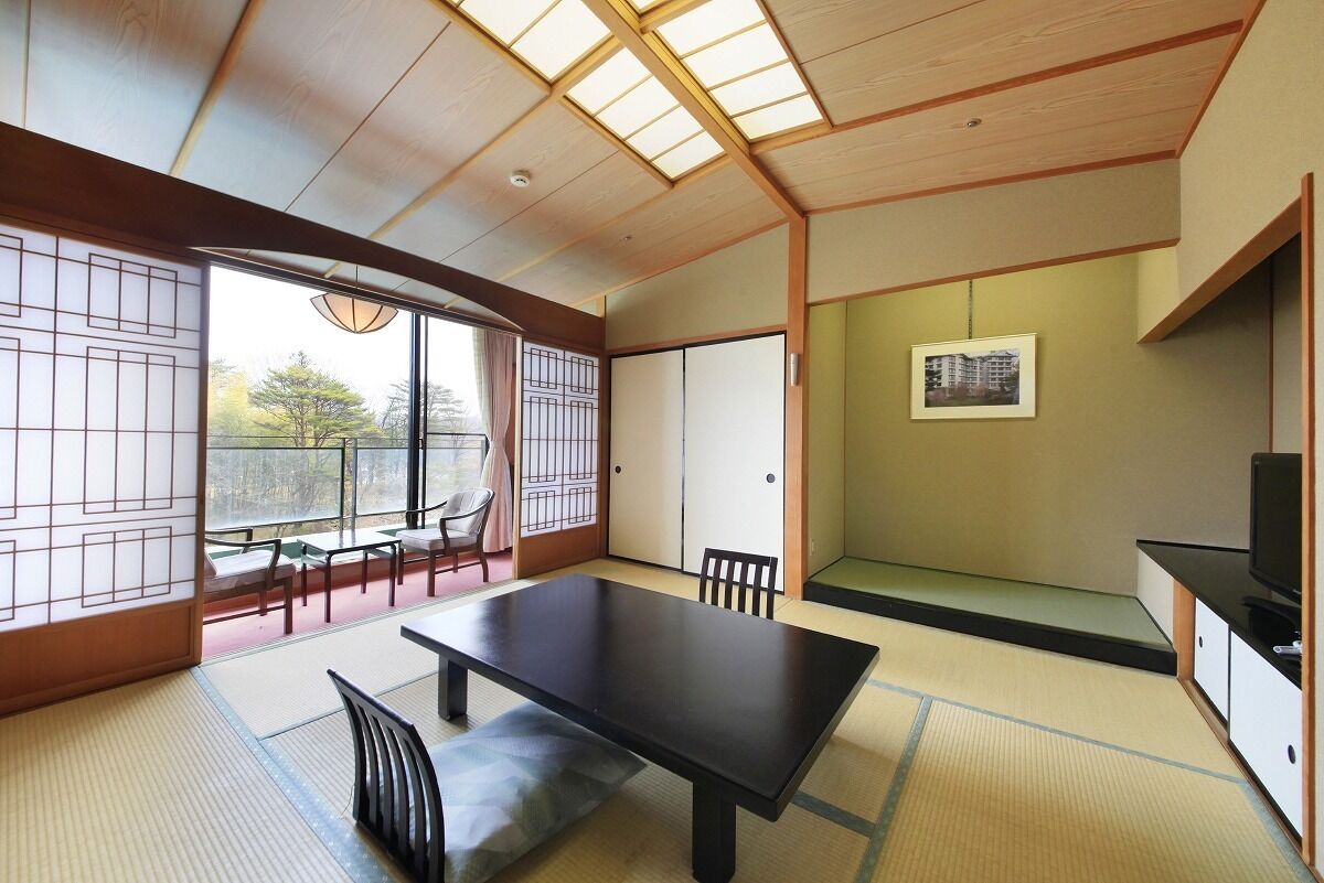 A traditional Japanese room with tatami flooring, a low table, chairs, a sliding door, and a television.