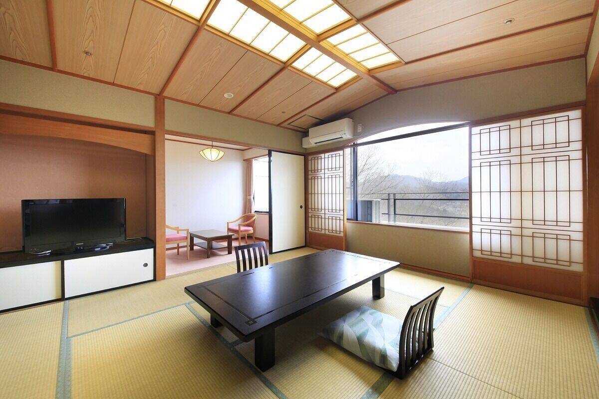 Una habitación japonesa tradicional con suelo de tatami, una mesa baja, un televisor y puertas correderas.