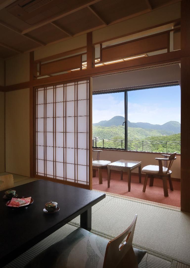 Una habitación japonesa tradicional con suelo de tatami, un divisor corredizo shoji y vistas a un paisaje montañoso.