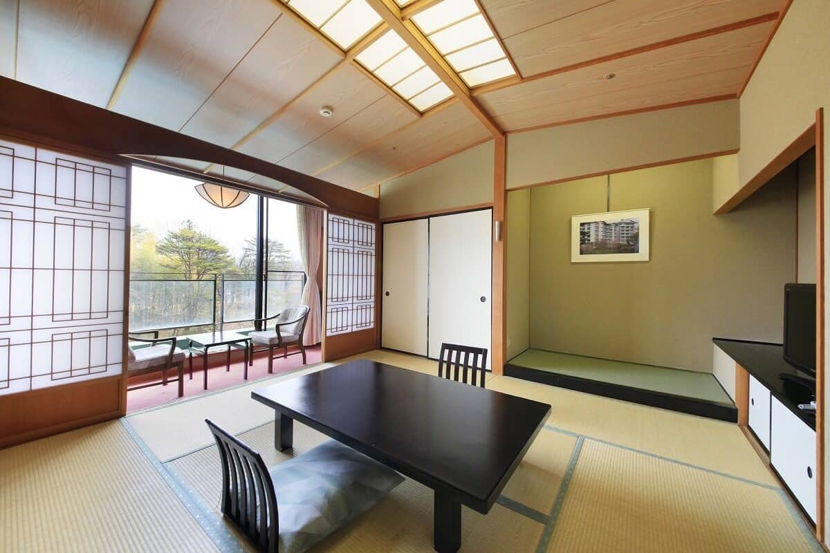 Una habitación japonesa tradicional con suelo de tatami, una mesa baja, sillas y una puerta corredera.