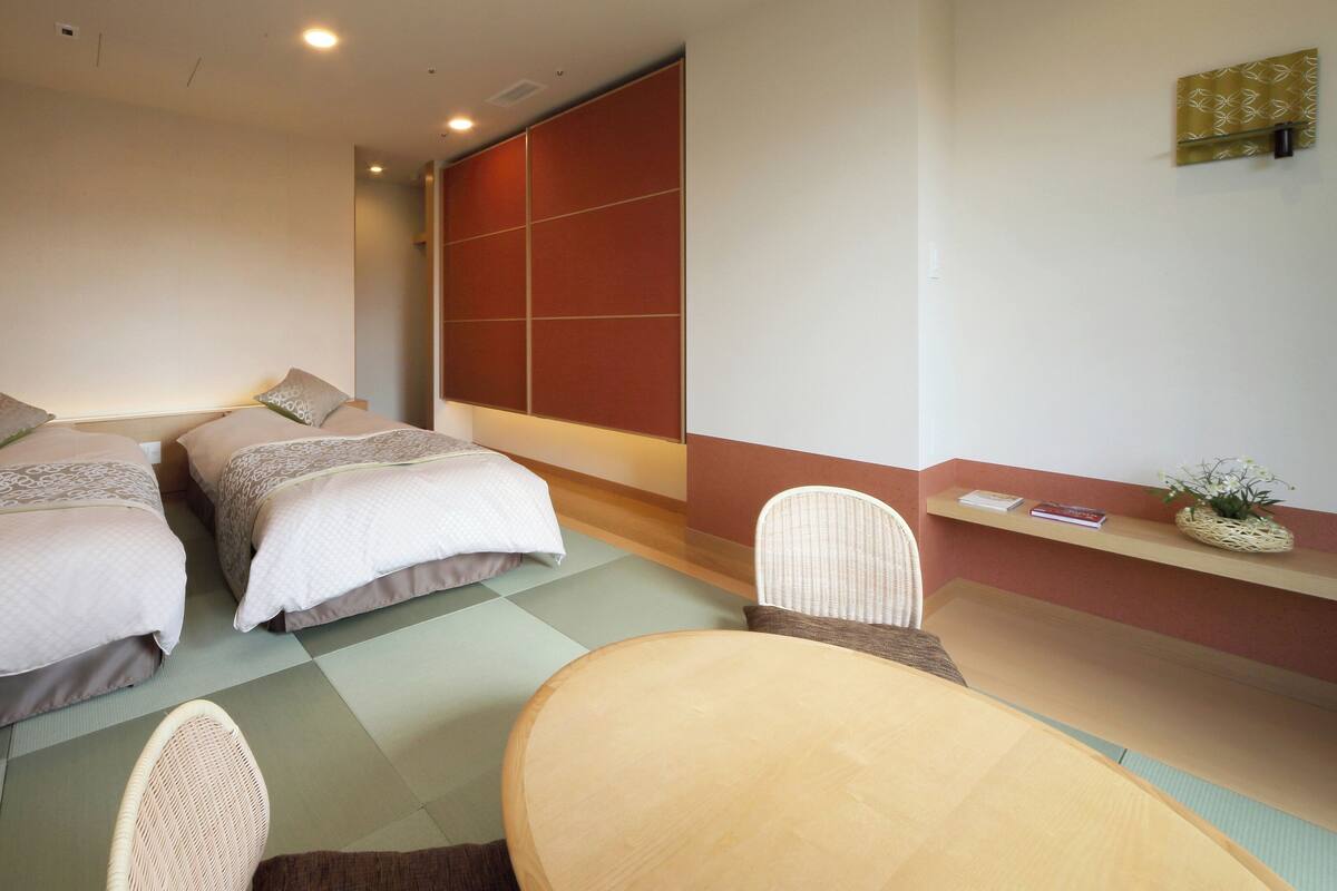 Una habitación de hotel con dos camas, una mesita pequeña y una silla.