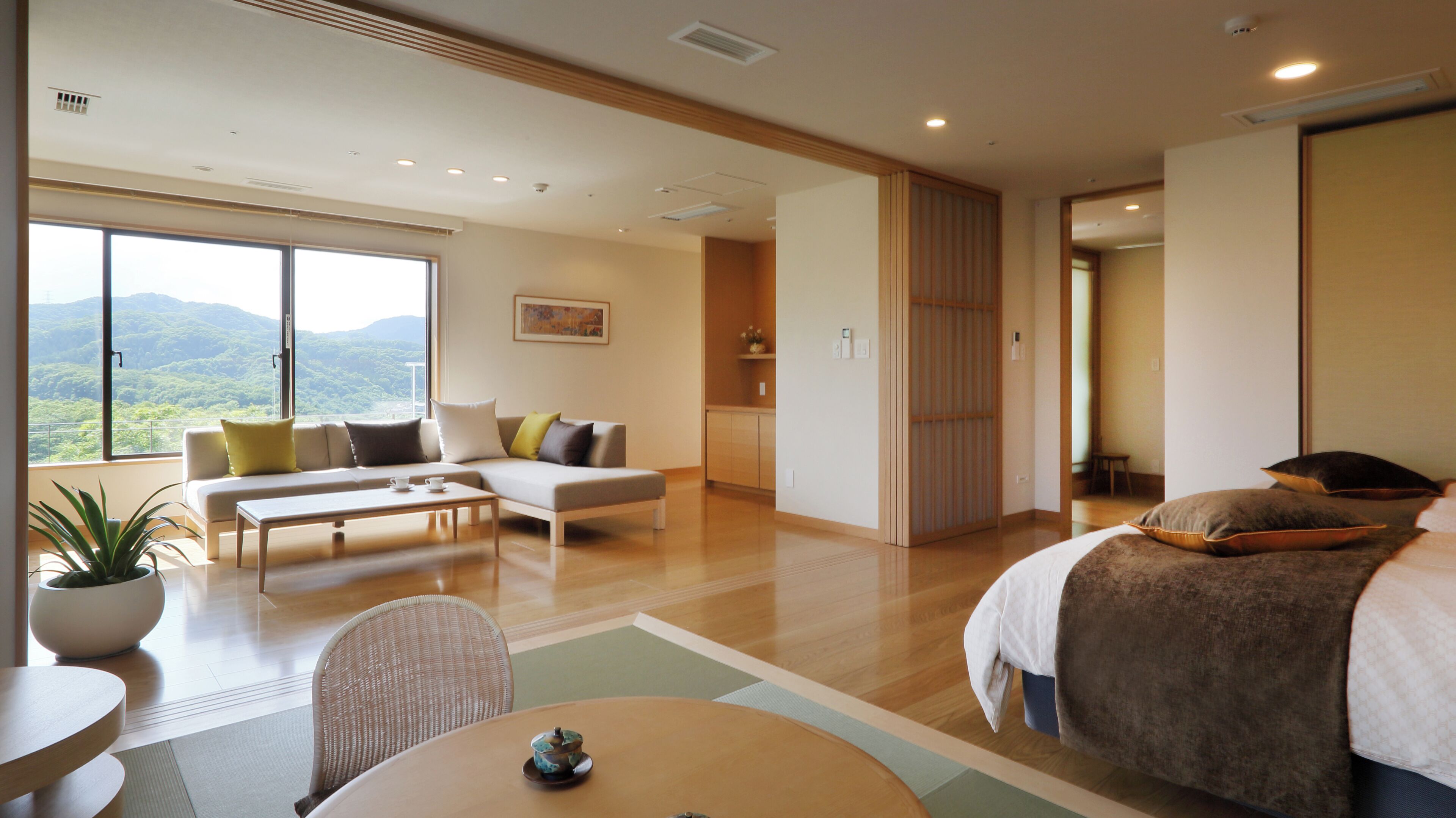 A modern hotel room with a sofa, a dining table, a bed, and a view of the outdoors.