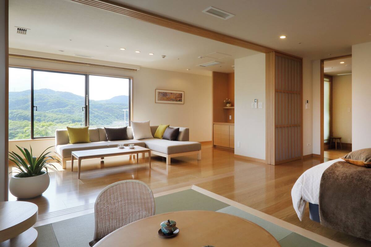 Habitación de hotel moderna con sofá, mesa de comedor, cama y vistas al exterior.