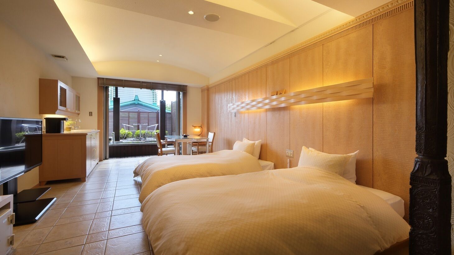 Habitación de hotel con dos camas, un escritorio, televisión y vistas al exterior.