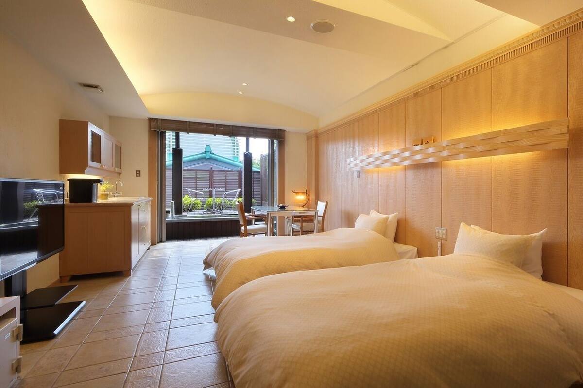 Habitación de hotel con dos camas, un escritorio, televisión y vistas al exterior.