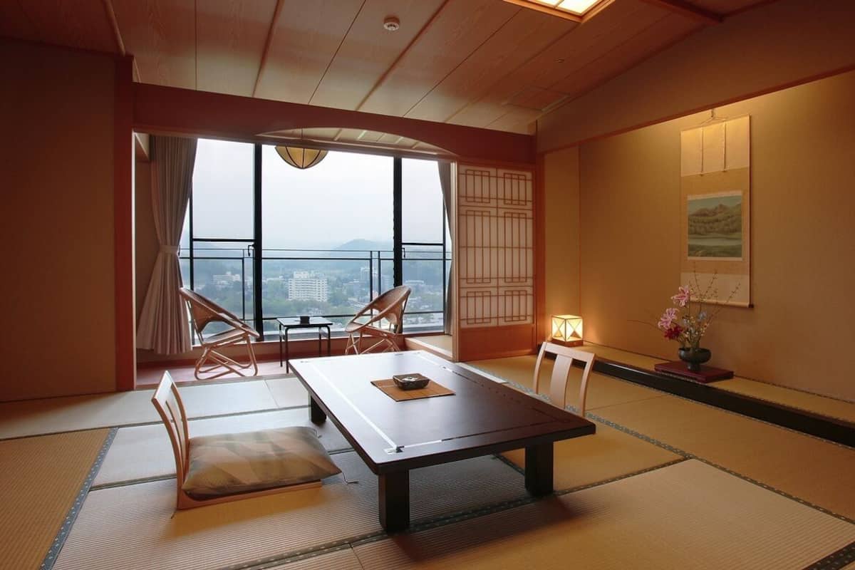 Una habitación japonesa tradicional con suelo de tatami, una mesa baja y vistas a la ciudad.