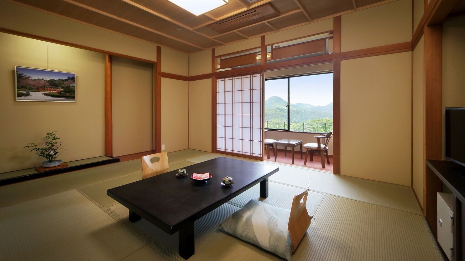 Una habitación tradicional japonesa con suelo de tatami, una mesa baja con cojín, una puerta corrediza con vistas y un televisor a la derecha.