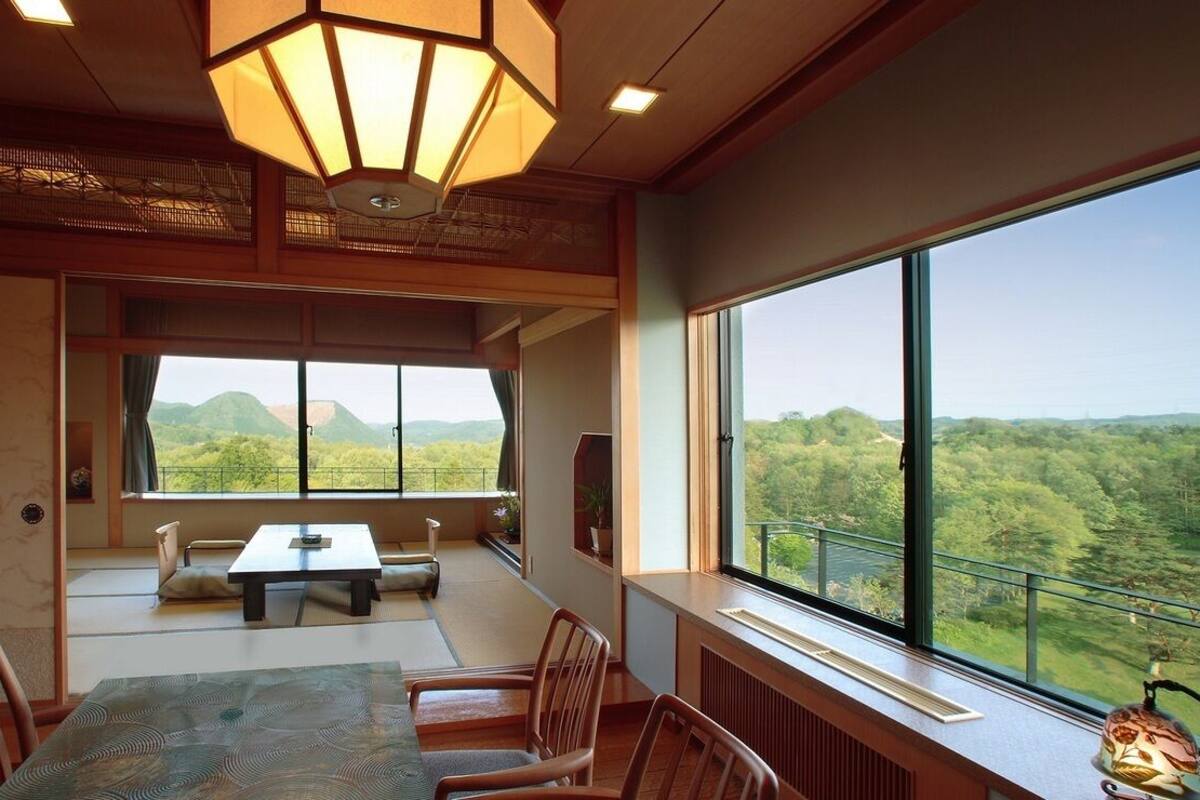 Una habitación con una mesa de comedor, sillas, un ventanal con vistas a zonas verdes y colinas, y una lámpara de techo de estilo tradicional.