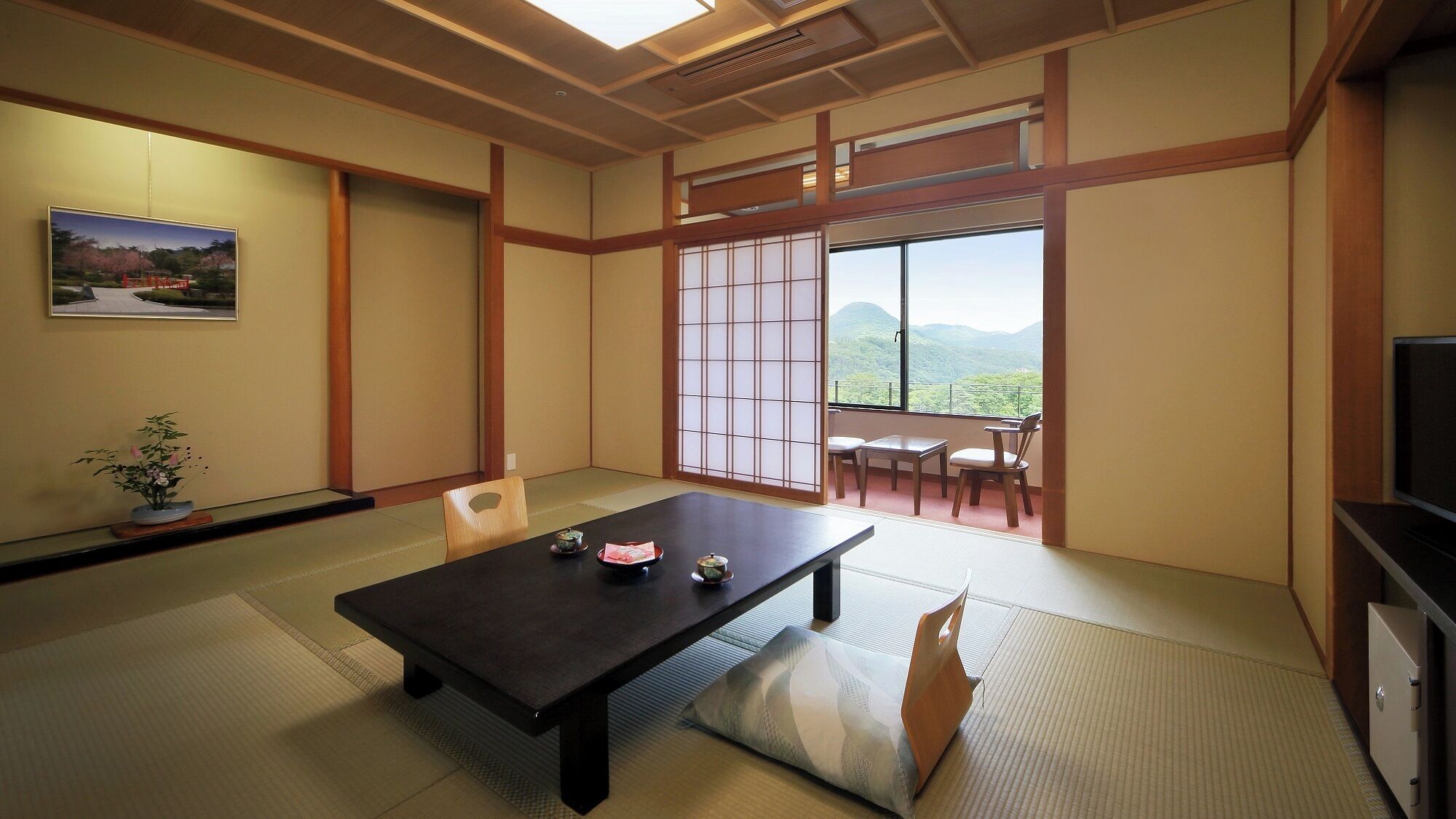 A traditional Japanese room with tatami flooring, a low table with cushions, sliding doors, and a view of a mountainous landscape.