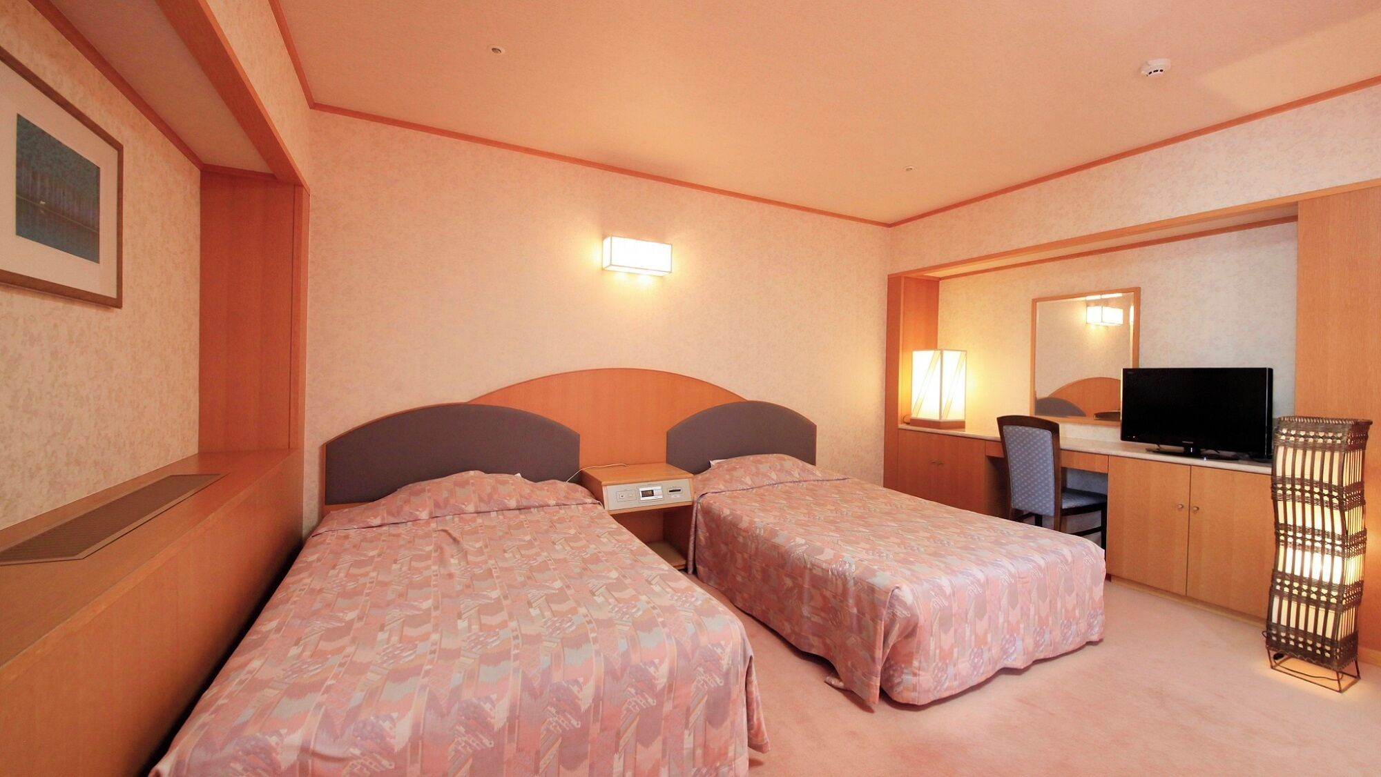 A hotel room with two beds, a desk with a television, a chair, and a lamp.