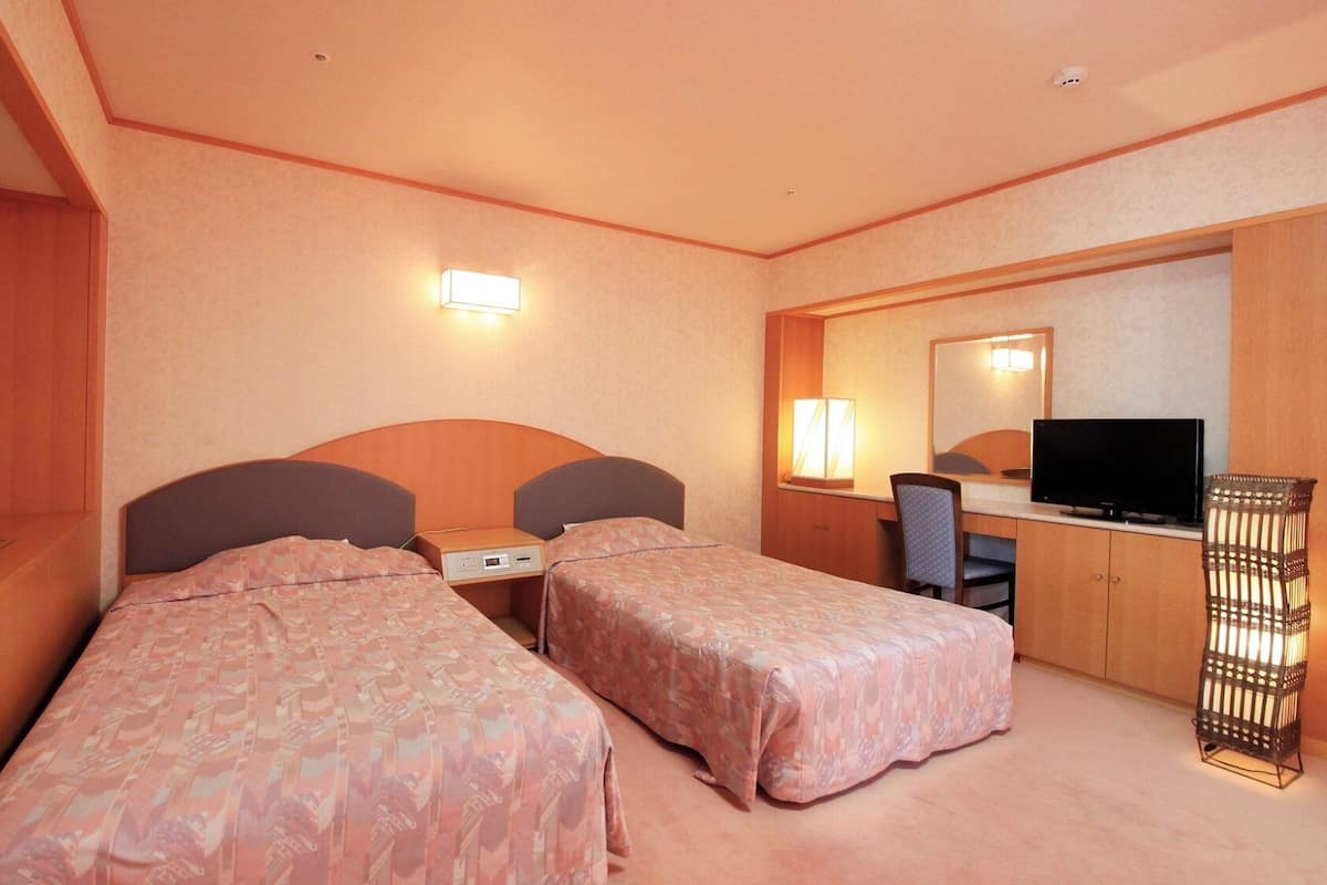 Una habitación de hotel con dos camas, un escritorio con televisor, una silla y una lámpara.