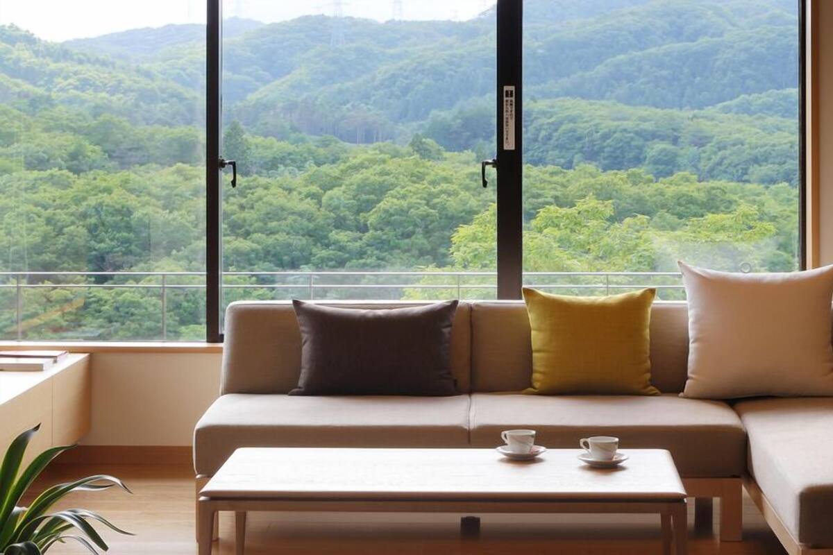 Una sala moderna con un sofá, cojines, una mesa de centro y vistas a una ladera boscosa.