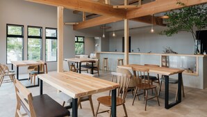 A modern interior with wooden tables and chairs, a kitchen area, and large windows. - Glanta Glamping Village (Sanda)