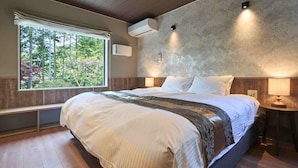 A bedroom with a large bed, a bench, a window with a view of trees, an air conditioning unit, and a wall-mounted light fixture. - Orando no Nikai (Aridagawa)