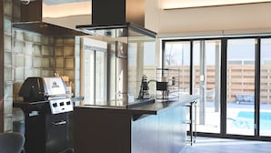 A modern kitchen with a built-in grill, large windows, and a view of a swimming pool. - Orando no Nikai (Aridagawa)